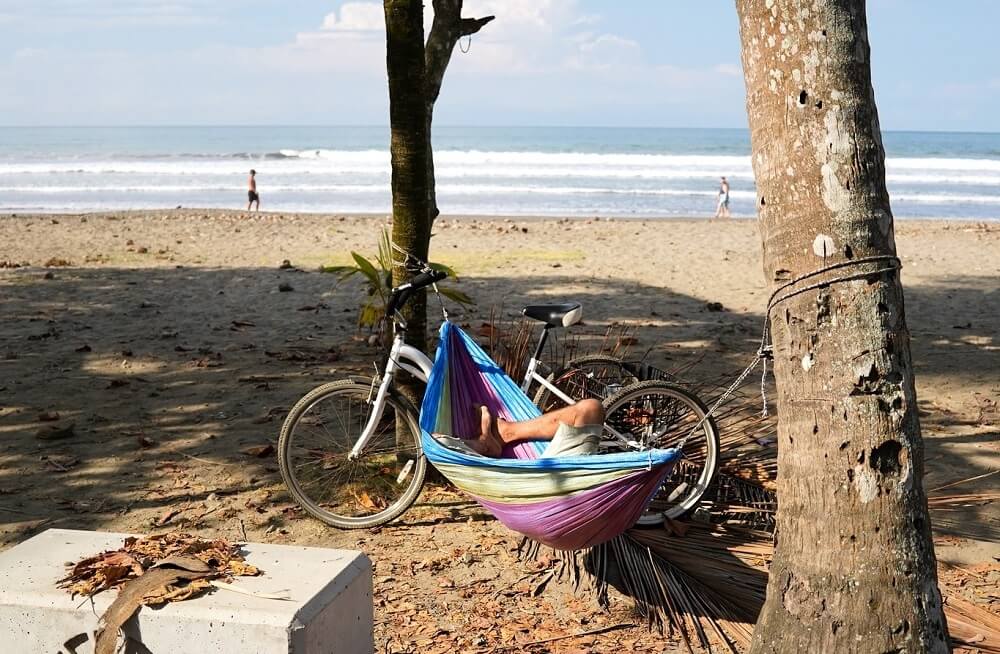 Člověk odpočívající v barevné houpací síti na písečné pláži v Kostarice